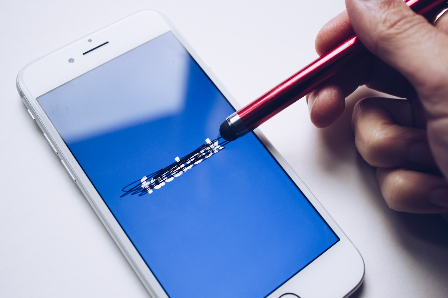 A mobile phone showing a Facebook logo, struck through several times, on blue background. To the right of it a hand holding a pen, which seems to have been used for striking the logo. Photo by Thought Catalog via Unsplash, https://unsplash.com/photos/tRL_Rkh6D8o